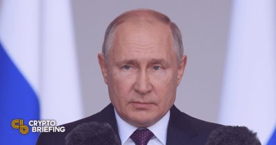 Vladimir Putin speaking at a podium, Russian flag partially visible in the background.