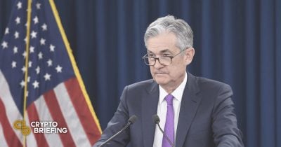 Federal Reserve Chairman Jerome Powell speaking at a podium with the U.S. flag in the background.