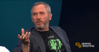 Brad Garlinghouse, CEO of Ripple, speaking during an interview, wearing a black XRP-themed t-shirt and a blue blazer.