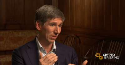 Matt Hougan speaking in an interview, gesturing with hands. The background features wooden paneling and chairs.