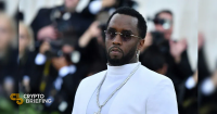 Sean "Diddy" Combs wearing a white suit and sunglasses at a formal event, with photographers in the background.