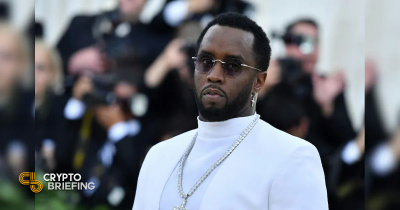 Sean "Diddy" Combs wearing a white suit and sunglasses at a formal event, with photographers in the background.