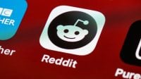 Reddit app icon on a smartphone screen displaying the alien mascot logo and name "Reddit" in white text against a red background.