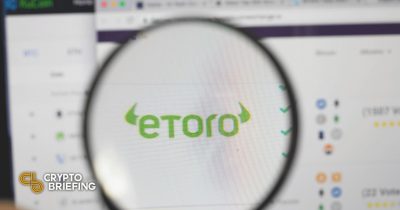 Lupa enfocando el logo de eToro en una pantalla de computadora borrosa, implicando análisis o revisión de la plataforma de trading eToro.