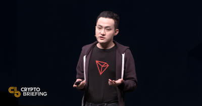 Justin Sun hablando en una conferencia de criptomonedas, vistiendo una camisa con el logo de Tron (TRX) y gesticulando con sus manos.