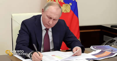 Vladimir Putin firmando documentos en su escritorio, con la bandera rusa al fondo y papeles visibles en su escritorio.